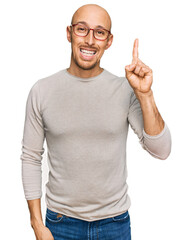 Naklejka premium Bald man with beard wearing casual clothes and glasses showing and pointing up with finger number one while smiling confident and happy.