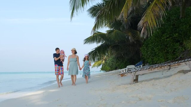 Young big family of four walking along tropical beach in sunny morning. Summer vacation and travel concept