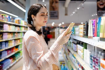 Portrait of Caucasian woman choosing cosmetic cream in grocery store. Shelves with food in...
