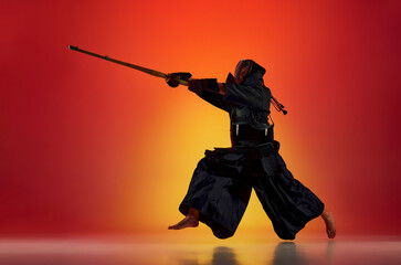 Man, professional kendo athlete in black uniform with sword, shinai training against gradient red...