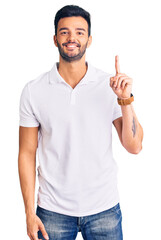 Young handsome hispanic man wearing casual clothes showing and pointing up with finger number one while smiling confident and happy.