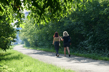 Two women walk along path in park among trees