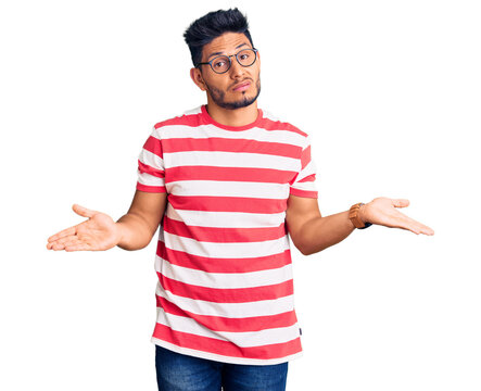 Handsome latin american young man wearing casual clothes and glasses clueless and confused with open arms, no idea concept.