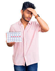 Handsome latin american young man holding heart calendar stressed and frustrated with hand on head, surprised and angry face