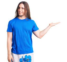 Young adult man with long hair wearing swimwear smiling cheerful presenting and pointing with palm of hand looking at the camera.