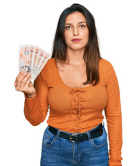 Beautiful hispanic woman holding 10 united kingdom pounds banknotes thinking attitude and sober expression looking self confident