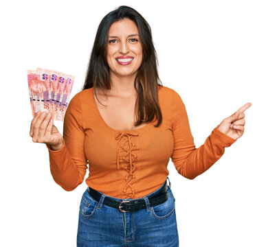 Beautiful hispanic woman holding south african 50 rand banknotes smiling happy pointing with hand and finger to the side