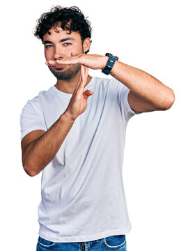 Hispanic young man with beard wearing casual white t shirt doing time out gesture with hands, frustrated and serious face