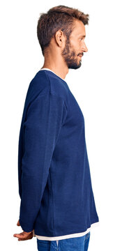 Handsome blond man with beard wearing casual sweater looking to side, relax profile pose with natural face and confident smile.
