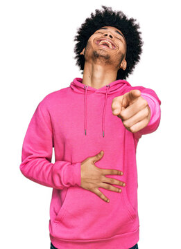 Young african american man with afro hair wearing casual pink sweatshirt laughing at you, pointing finger to the camera with hand over body, shame expression