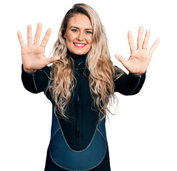 Young blonde woman wearing diver neoprene uniform showing and pointing up with fingers number ten...