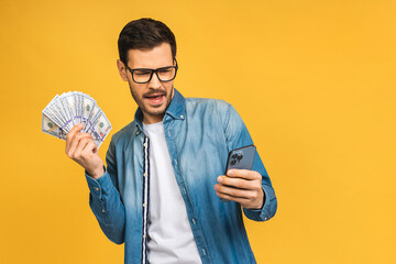 Happy winner! Excited man in casual holding lots of money in dollar currencys and using phone in...