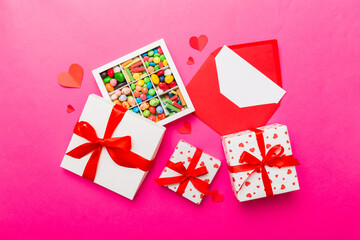 Red envelope with candy and gift box and Valentines hearts on colored background. Flat lay, top view. Romantic love letter for Holiday concept