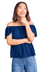 Young beautiful chinese girl wearing casual clothes with hand on chin thinking about question, pensive expression. smiling with thoughtful face. doubt concept.