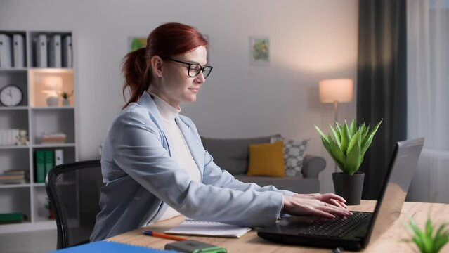 young woman in glasses doing job remotely making notes in notebook while sitting at laptop in room