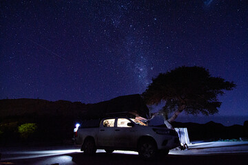 Fototapeta na wymiar Milky way over a tent located on the roof of a pickup car in the Namib desert in Namibia. Night photo with many stars.