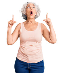 Senior grey-haired woman wearing casual clothes amazed and surprised looking up and pointing with fingers and raised arms.