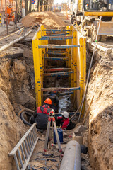 Workers working at deepening supported by trench box with pipe bedding pea gravel during installation of drainage pipe.