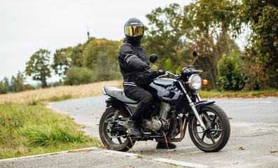 Fototapeta na wymiar motorcyclist in motorcycle clothing and a helmet on an old motorcycle cafe racer in the summer on the road