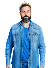 Hispanic man with beard wearing king crown with serious expression on face. simple and natural looking at the camera.