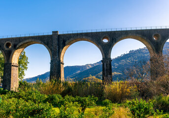 Fototapeta premium nice old vintage bridge with big arcs and columns among nature with green garneds and blue sky , european old concept landscape