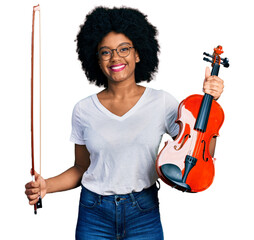 Young african american woman playing violin smiling with a happy and cool smile on face. showing...