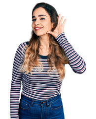 Obraz na płótnie Canvas Beautiful hispanic woman wearing casual striped shirt smiling with hand over ear listening an hearing to rumor or gossip. deafness concept.