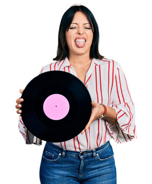 Young hispanic girl holding vinyl disc sticking tongue out happy with funny expression.
