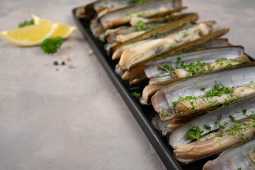 dish of razor clam grilled with garlic, parsley, olive oil and lemon slice on wood table