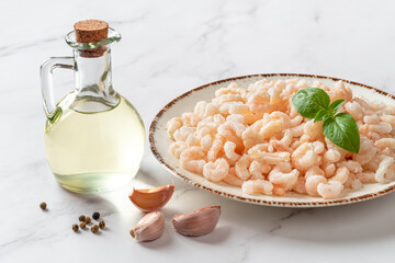 Frosen shrimps on a plate over marble countertop. Cooked peeled prawn tails, olive oil and garlic prepared for cooking. Sea crustacean for low calorie healthy meals. Seafood recipe.