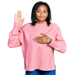 Beautiful hispanic woman wearing casual winter sweater swearing with hand on chest and open palm,...