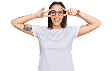 Obraz na płótnie Canvas Young hispanic woman wearing casual white t shirt doing peace symbol with fingers over face, smiling cheerful showing victory
