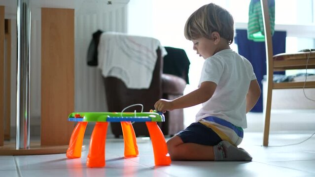 Candid little boy playing with table toy drawing board at home floor. Childhood development lifestyle
