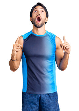 Handsome hispanic man wearing sportswear amazed and surprised looking up and pointing with fingers and raised arms.