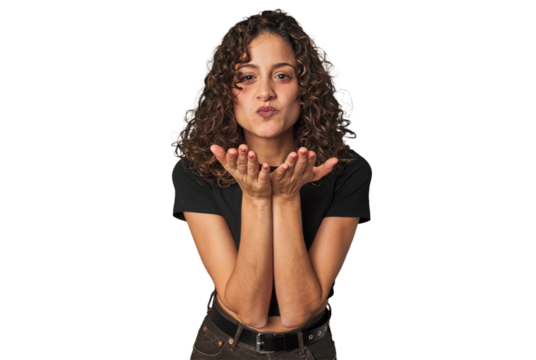 Radiant young woman with stunning curls folding lips and holding palms to send air kiss.