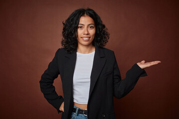 A young business colombian woman showing a copy space on a palm and holding another hand on waist.
