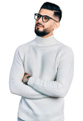 Young arab man with beard wearing elegant turtleneck sweater and glasses looking to the side with...
