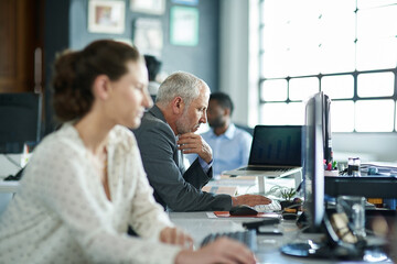 Obraz premium Getting down to work. Shot of a group of coworkers sitting at their workstations in an office.