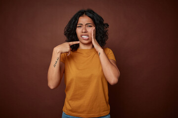 Young colombian curly hair woman isolated on brown background having a strong teeth pain, molar ache.