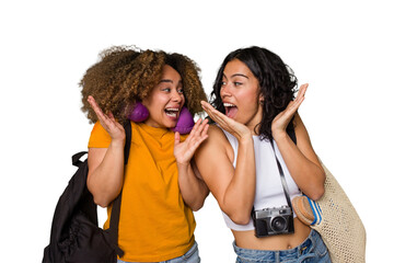 Two diverse friends on a beach vacation with vintage camera, beach bag, and travel pillow surprised and shocked.