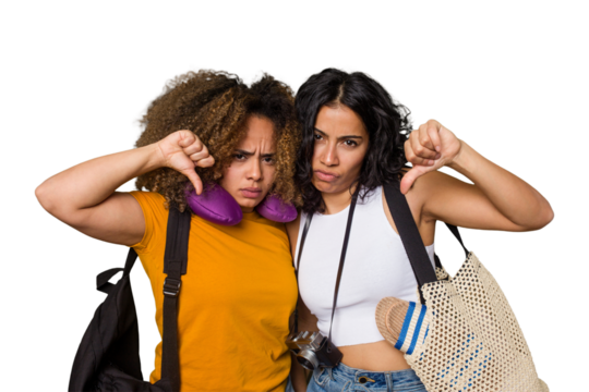 Two diverse friends on a beach vacation with vintage camera, beach bag, and travel pillow showing a dislike gesture, thumbs down. Disagreement concept.