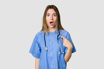 Young female nurse in uniform with stethoscope, symbol of care and dedication to patients pointing...