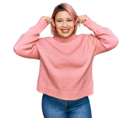 Hispanic woman with pink hair wearing casual winter sweater smiling pulling ears with fingers, funny gesture. audition problem