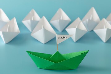 Leadership, teamwork and courage concept. Green paper boat on white paper boats on blue background.