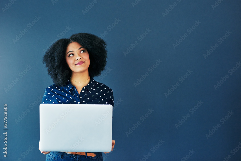 Poster Social media never fails to tickle the mind. Studio shot of an attractive young woman looking thoughtful while using a laptop against a blue background.