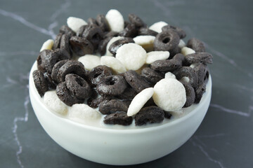 pouring milk into chocolate cereal corn flakes in a bowl on table 