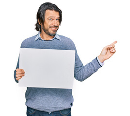 Middle age handsome man holding blank empty banner smiling happy pointing with hand and finger to the side