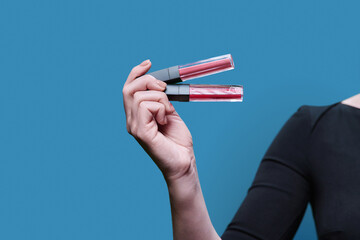 Close-up of two trendy lip glosses in hand, on blue background