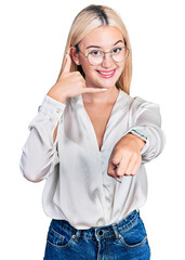 Beautiful blonde woman wearing elegant shirt and glasses smiling doing talking on the telephone...