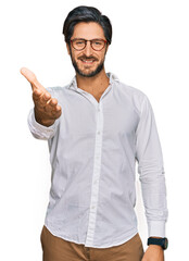Young hispanic man wearing business shirt and glasses smiling friendly offering handshake as greeting and welcoming. successful business.